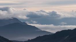 transcendent holistic meditation, enlightened expression, journeying inward, photorealistic, secluded mountain retreat, highly detailed, clouds drifting placidly, muted purples and grays, ethereal lighting, shot with a panoramic lens.